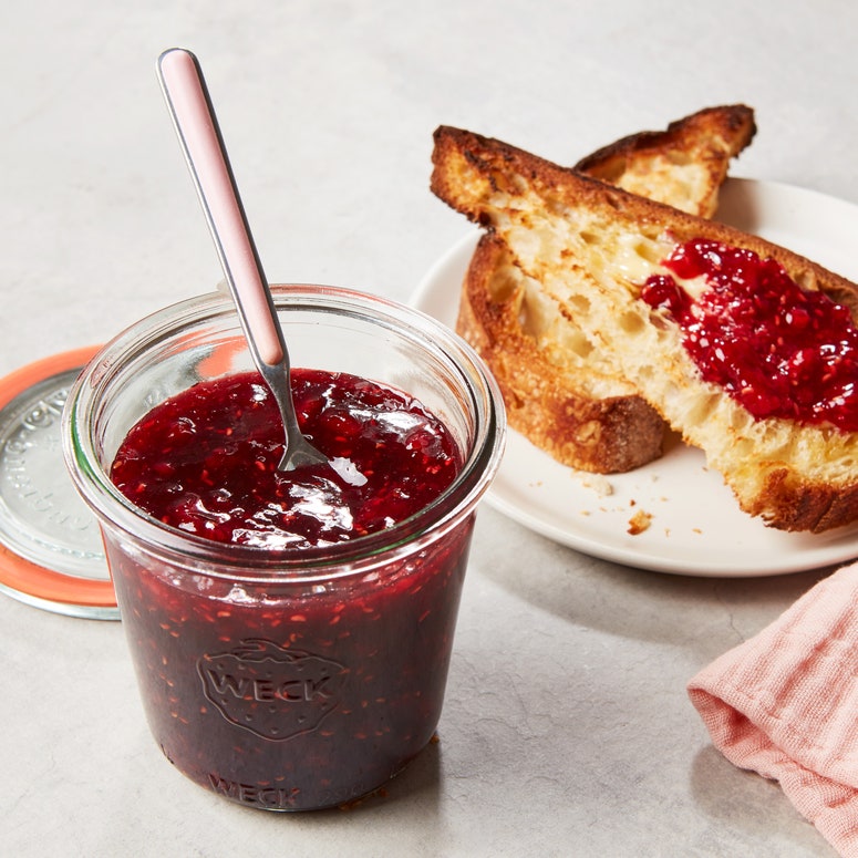 A jar of raspberry jam next to a plate of toast