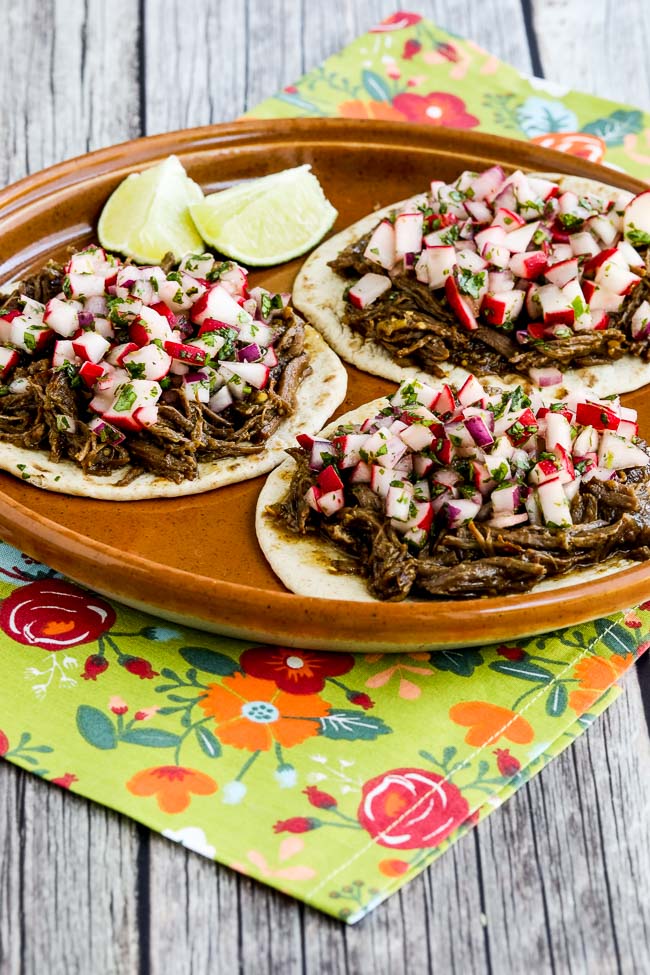 Spicy Shredded Beef Street Tacos shown on terra cotta plate with colorful napkin