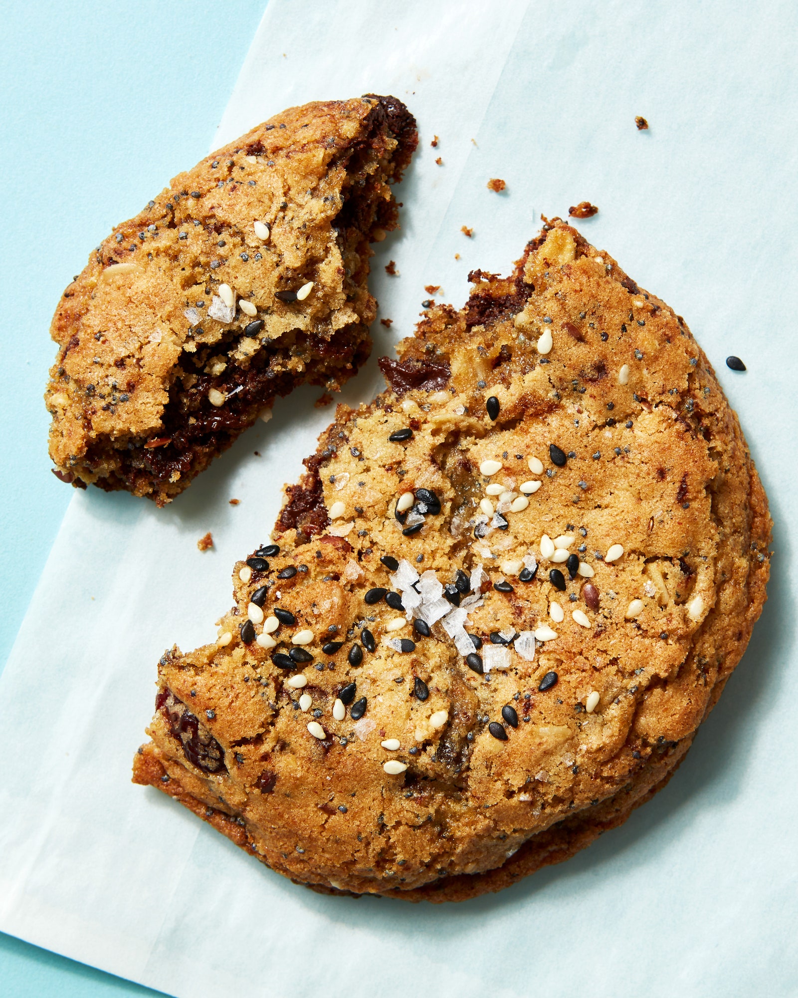 A cookie with chocolate chips walnuts cherries sesame and black sesame seeds in a wax paper bage.