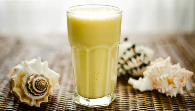 Pina colada smoothie on wicker tray with shells