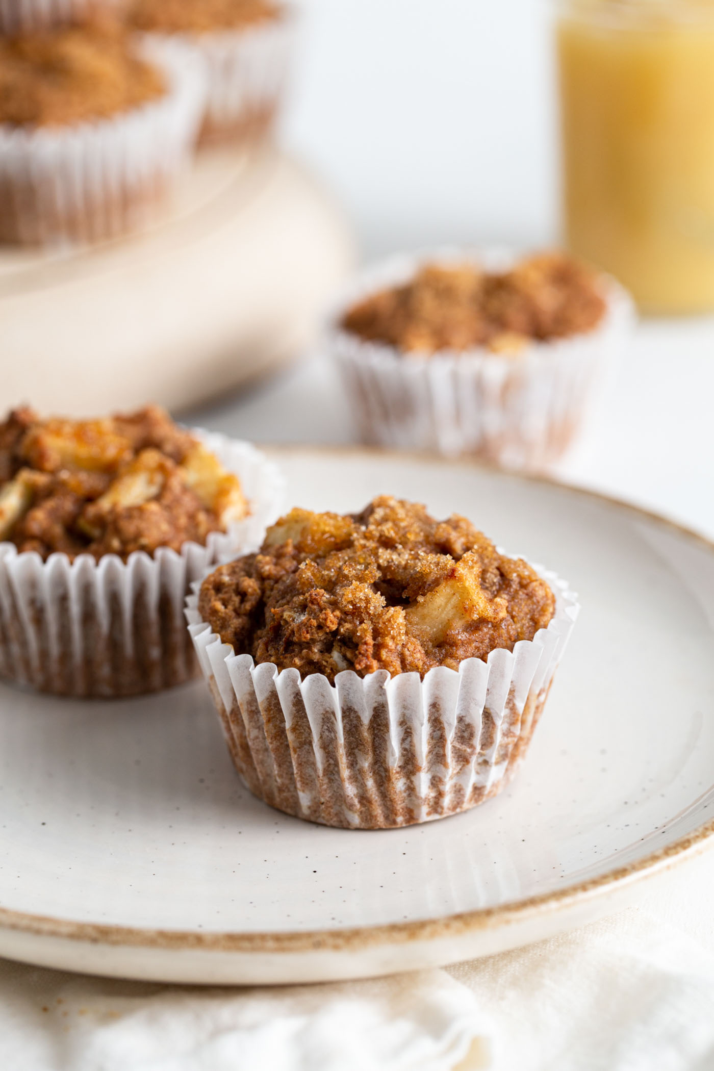 Two applesauce muffins on a plate. More muffins in background.