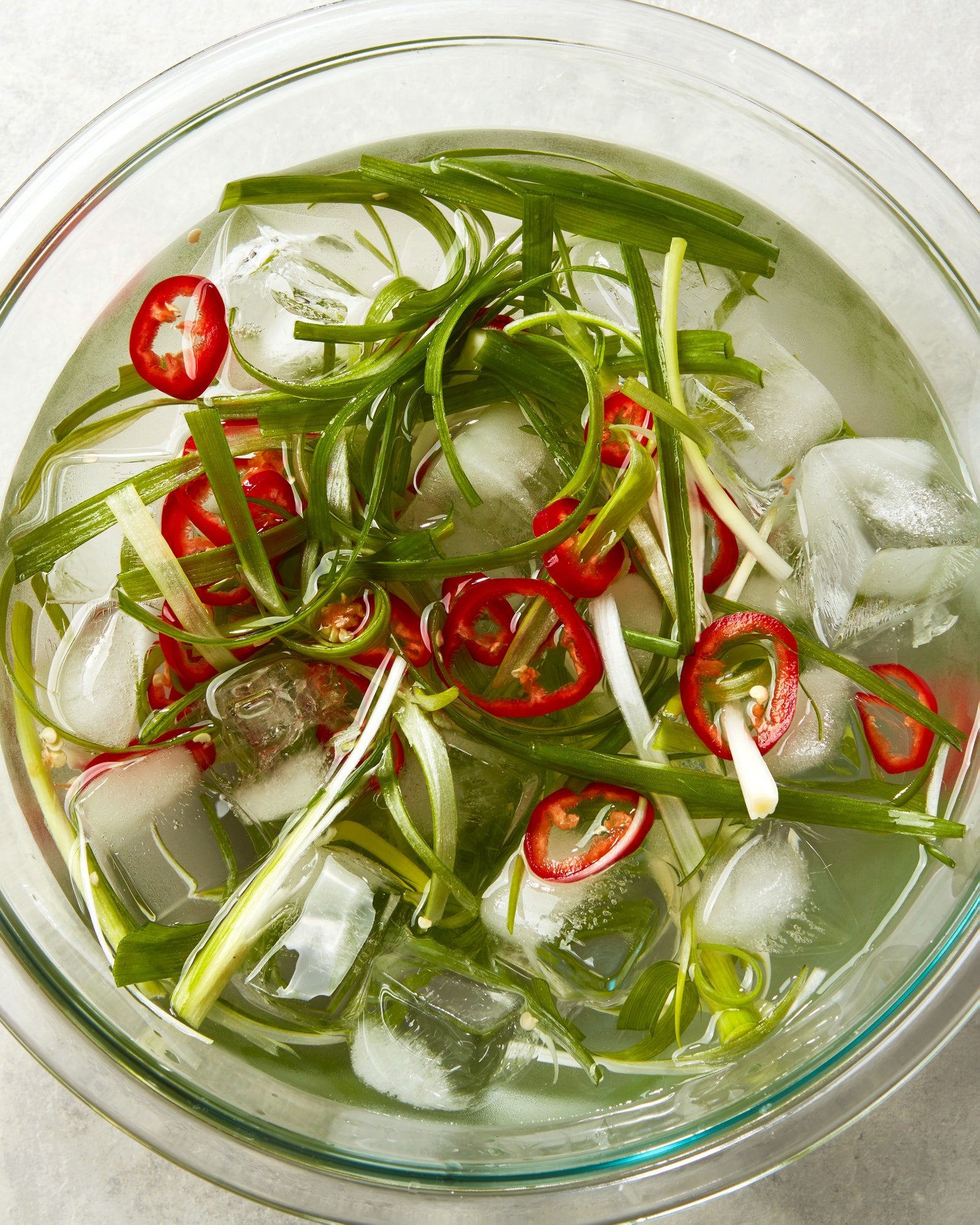 Scallions and fresno chili slices in a ice bath.