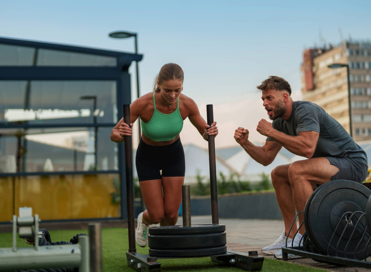 woman doing sled push workout at outdoor gym with trainer cheering her on