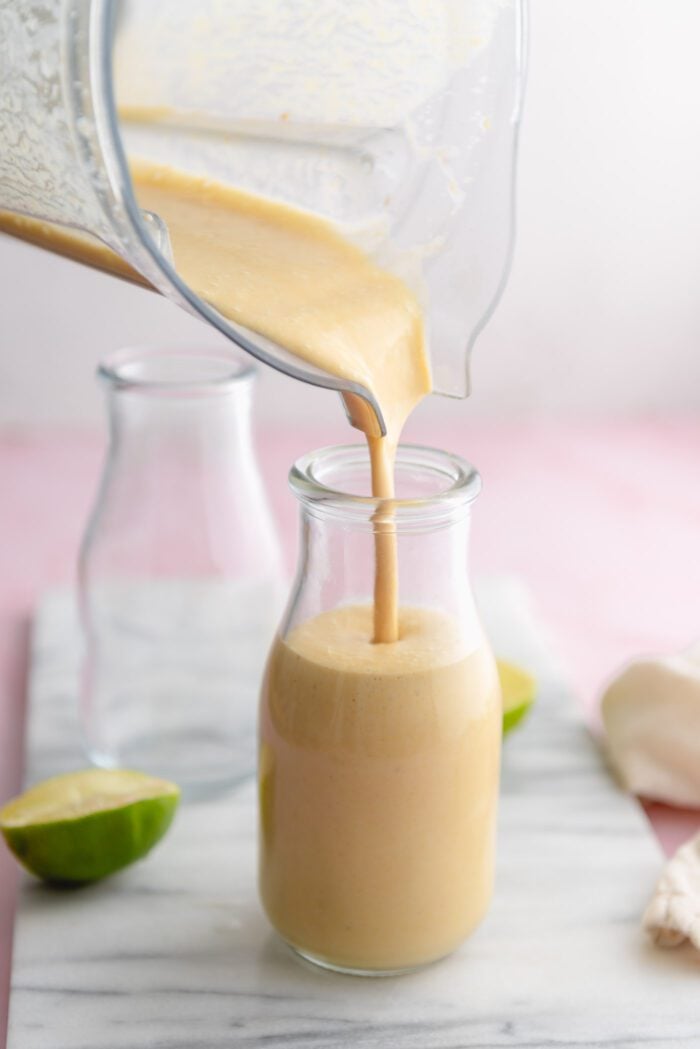 Pouring a mango smoothie from a blender into a glass jar.