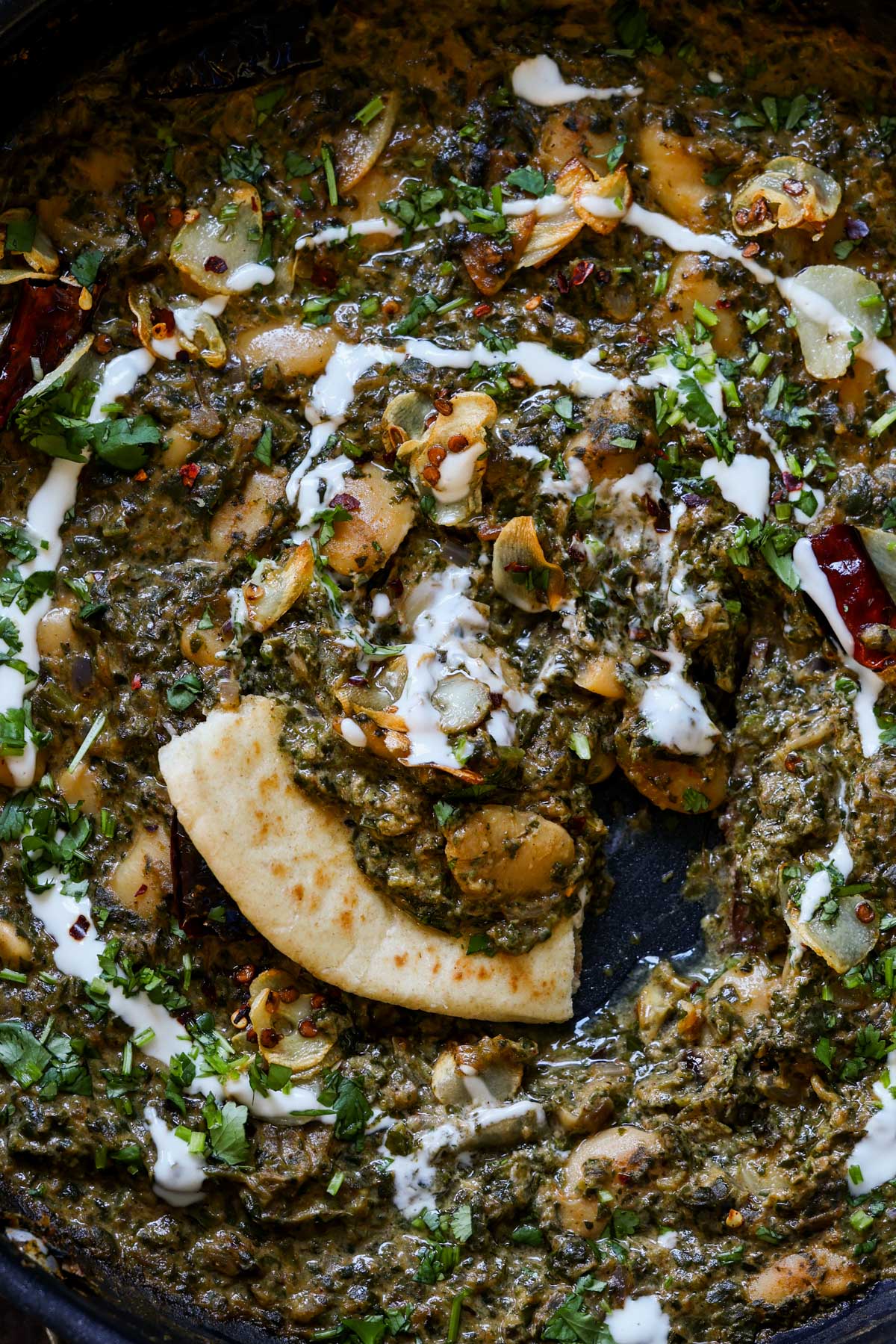 saag butter beans in the pan with a piece of flatbread