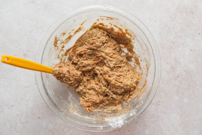 Raw carrot and zucchini muffin batter mixed in a mixing bowl with a wooden spoon in it.