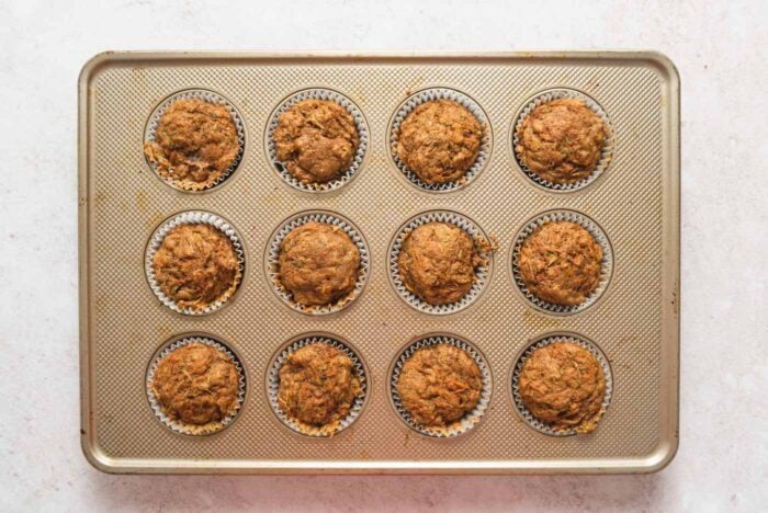 12 baked carrot zucchini muffins in a muffin pan.