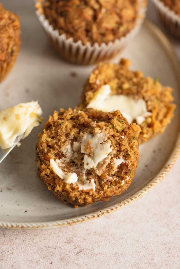 A carrot zucchini muffin cut in half and spread with butter on a plate.