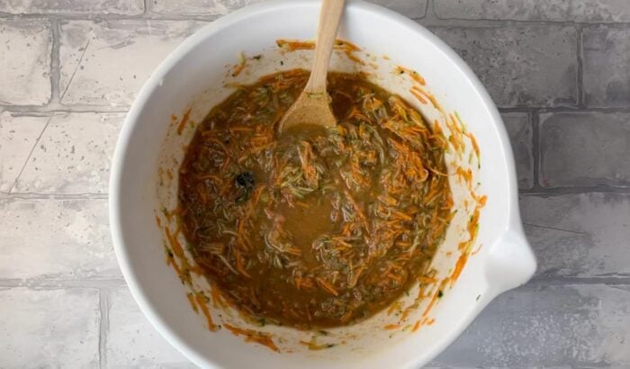 Raw carrot zucchini muffin batter in a mixing bowl with a wooden spoon.