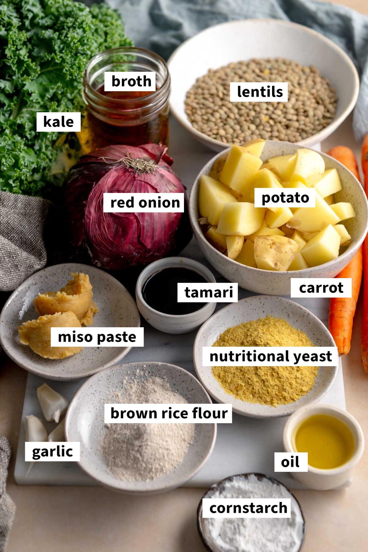 All of the ingredients for making a vegan lentil nourish bowl with roasted carrots and onion, kale, potato and a miso gravy sauce.