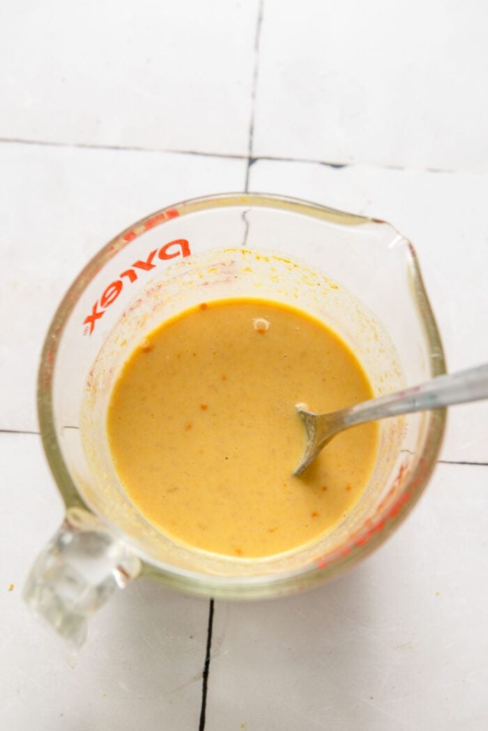 Creamy, yellow sauce in a glass measuring cup with spoon in it.