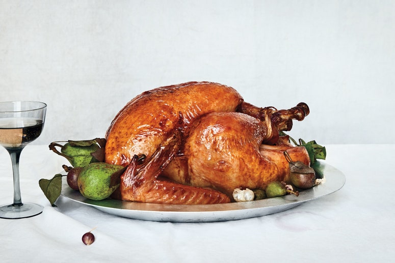 Side view of a whole roasted dry-brined turkey on a platter, decorated with fresh pears and garlic.