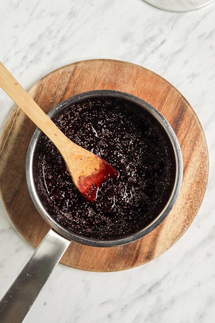 Mashed blueberries and chia seeds in a saucepan on a cutting board.