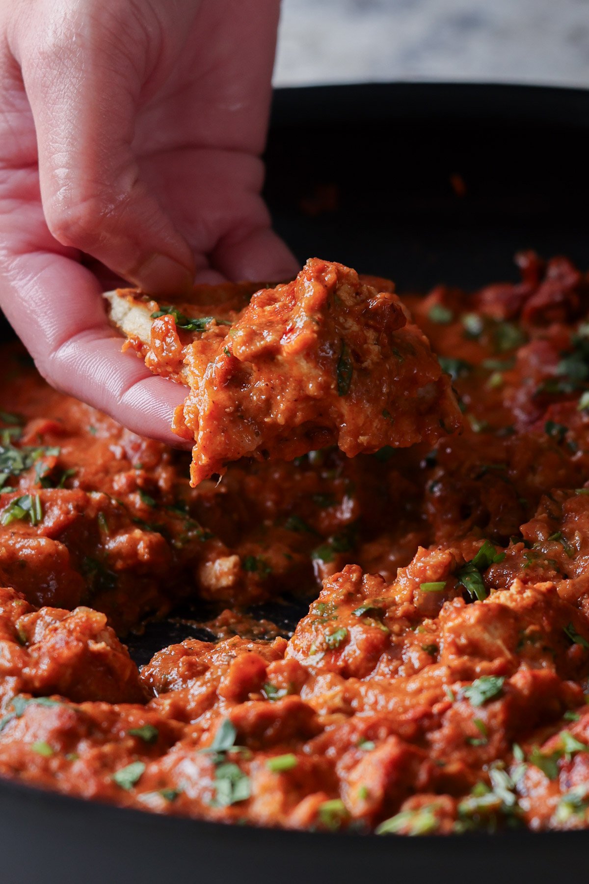 hand scooping up chicken angara with a piece of naan