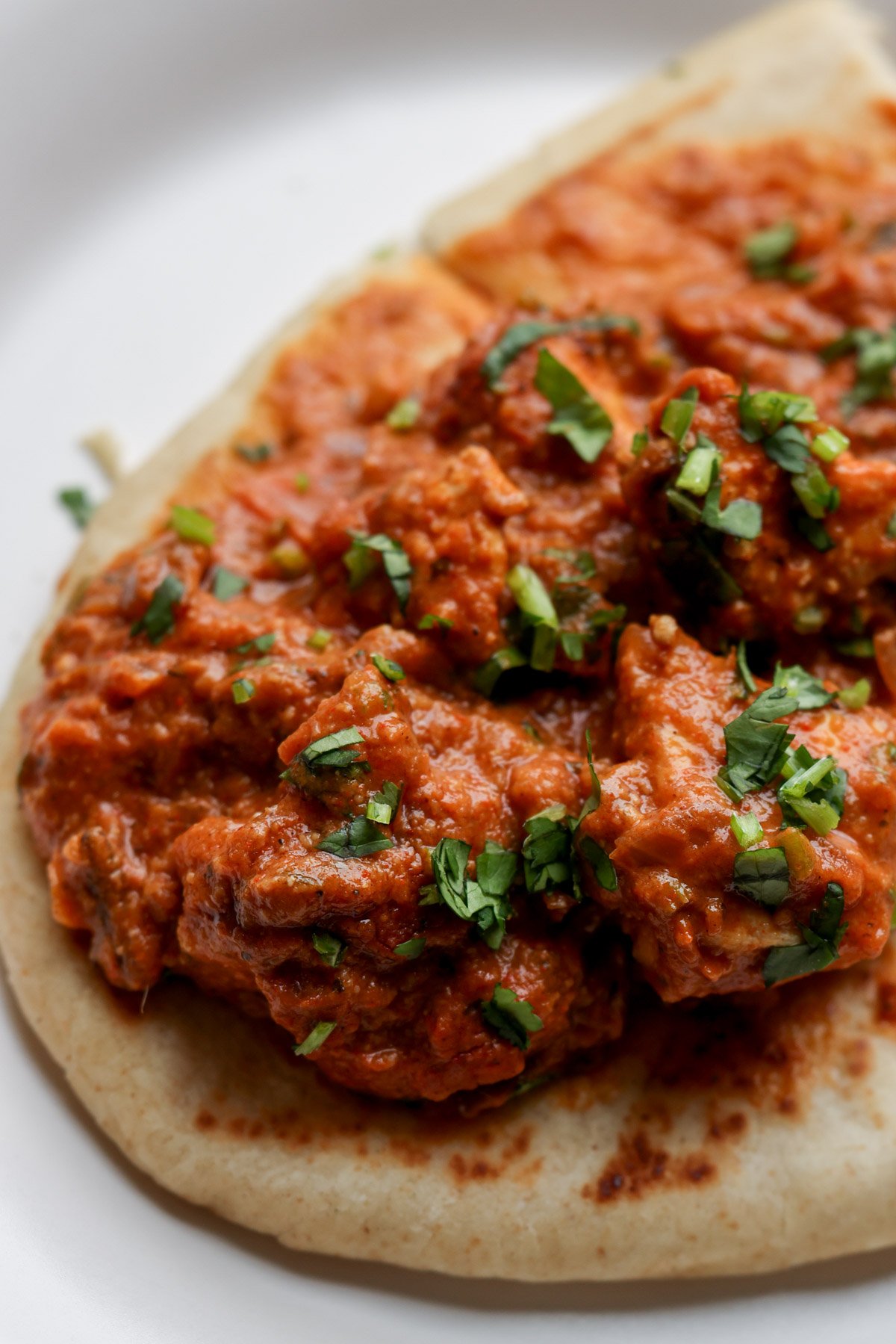 close-up of flatbread with chicken angara on top on a plate