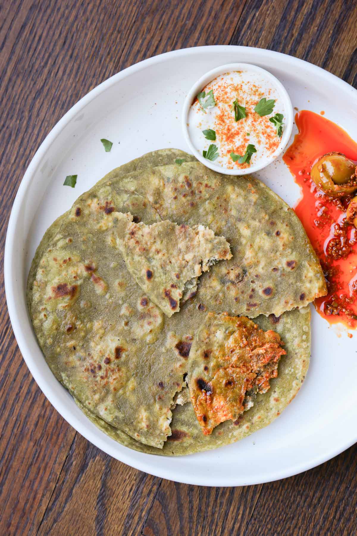 spinach paratha on a plate with raita and Indian pickle