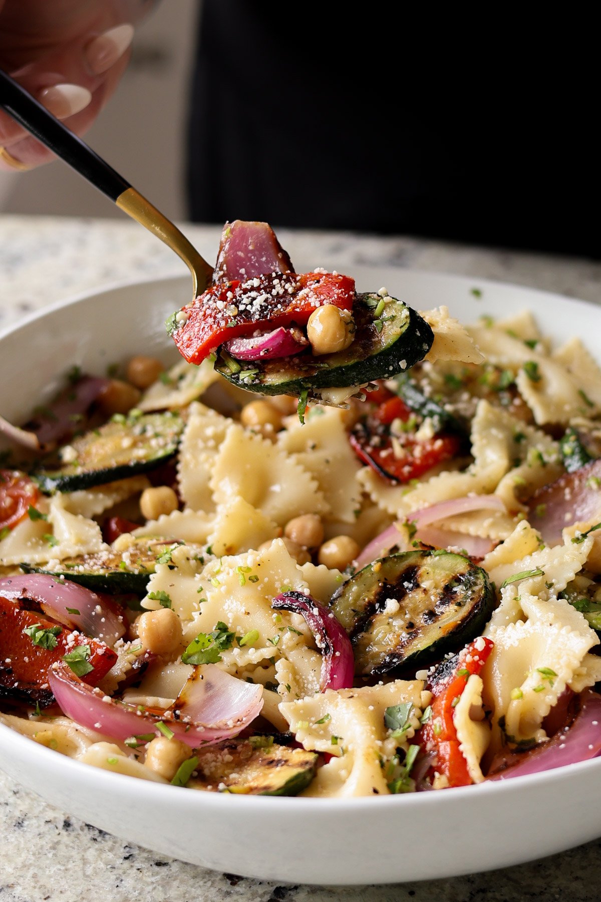spooning a bite of summer pasta salad with grilled vegetables