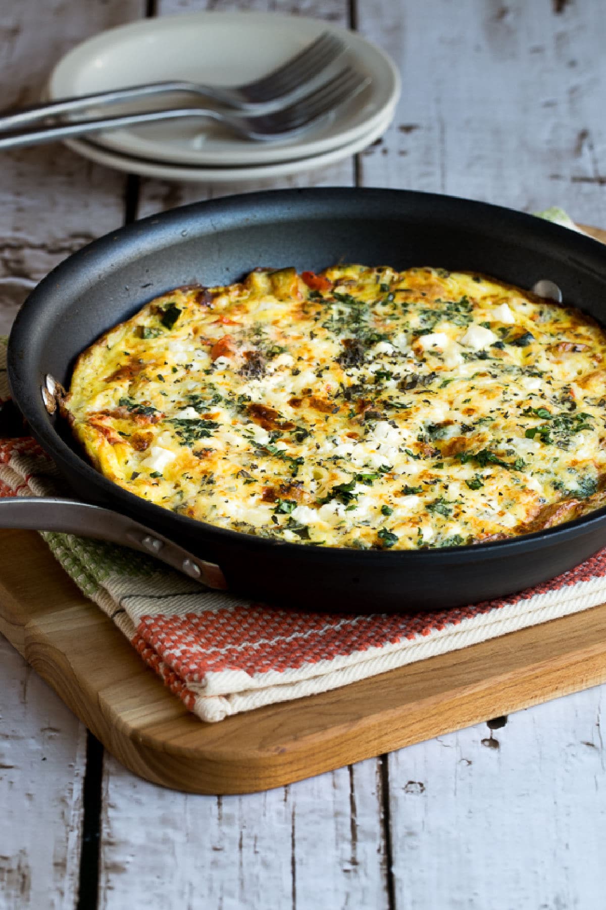 Greek Frittata shown in frittata pan with plates and forks in the background