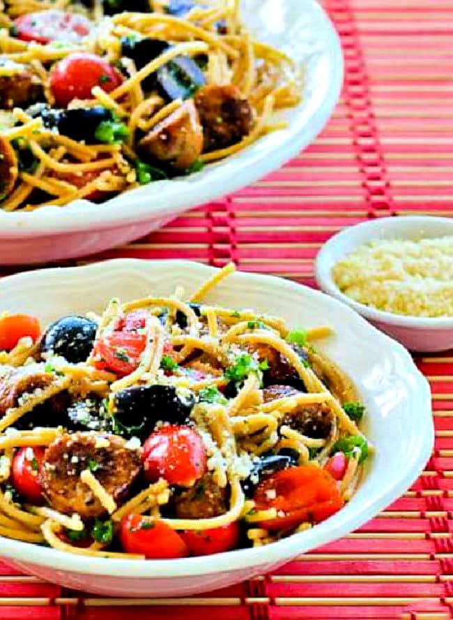 Spaghetti Pasta Salad in two bowls on red mat with Parmesan on the side.