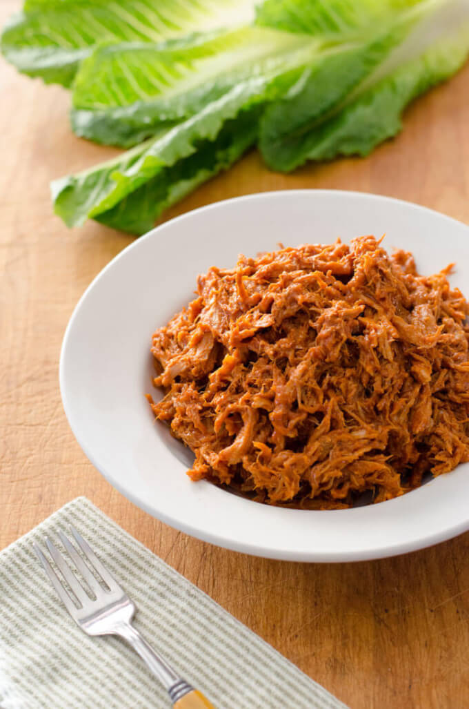 Crockpot pulled pork in white bowl with lettuce, fork and napkin.